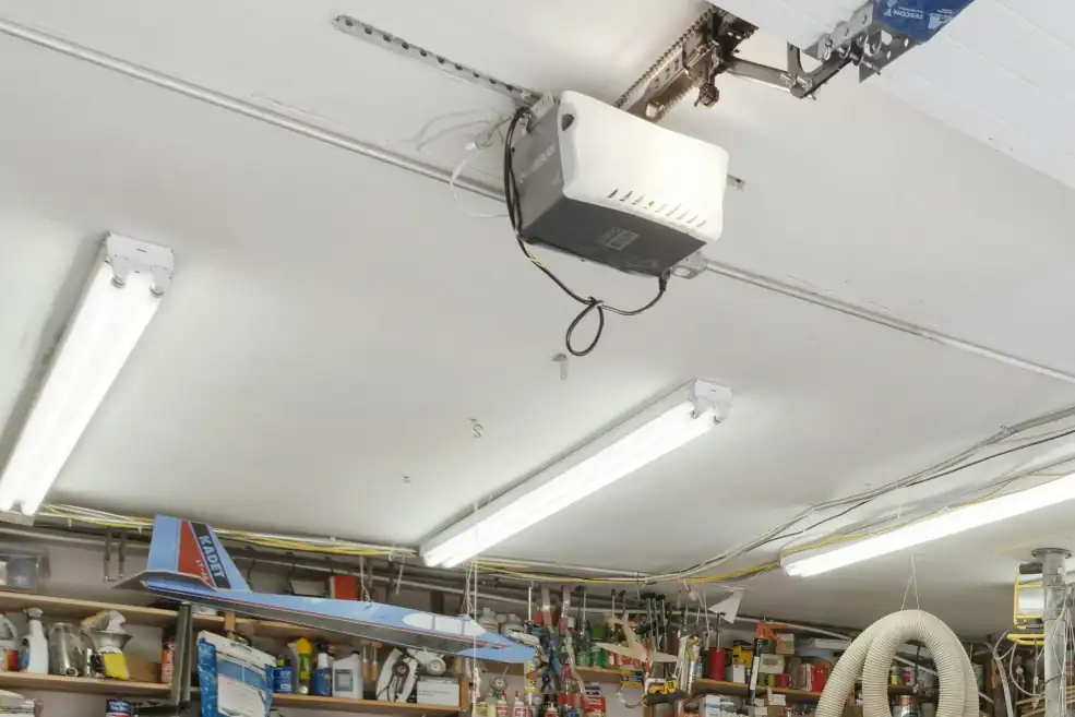 Ceiling-mounted garage door opener beside a raised sectional door in a workshop.