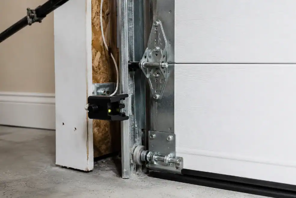 Close-up of garage door safety sensor, track, roller, and hinge hardware