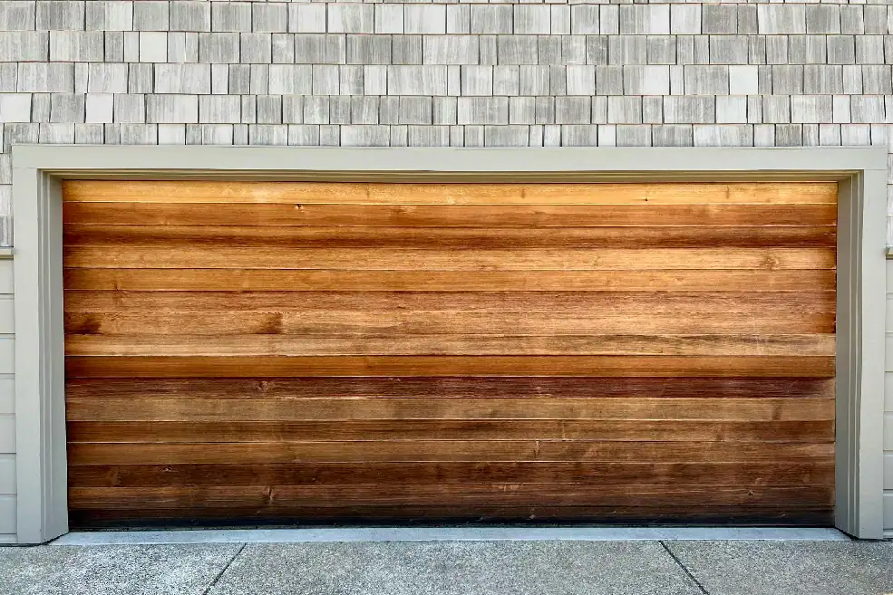 Closed wooden garage door beneath gray shingle siding.
