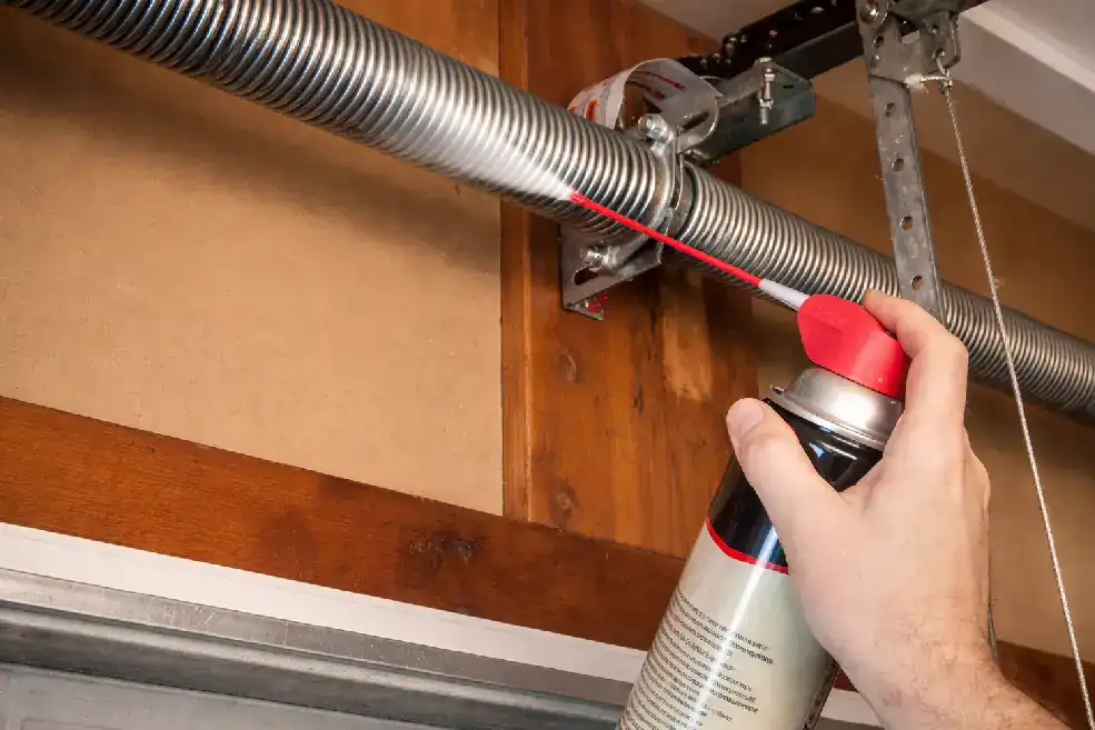 person spraying lubricant on garage springs.webp